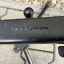 Detail černé kovové části hudebního příslušenství, pravděpodobně stojanu. Na povrchu je vyražen nápis Made in Germany. Povrch vykazuje drobné škrában…