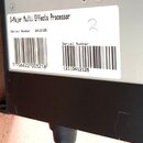 Detailní záběr na bílou papírovou nálepku s informacemi o zařízení, která je nalepena na šedém a černém povrchu. Na nálepce je uveden text G-Major Mu…