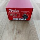 Červený hranatý přístroj s nápisem Weber a MINI MASS. Na přední straně jsou přepínače označené jako IMPEDANCE (8Ω, 16Ω, 4Ω), NORMAL a TREBLE (6db, 0d…
