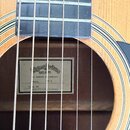 Detail akustické kytary s viditelným hmatníkem a otvorem rezonanční desky. Uvnitř korpusu je nalepený štítek s nápisy „Sigma Guitars“, „EST. 1970“, „…