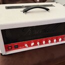 Bílý kytarový kombo zesilovač s červeným ovládacím panelem a černou mřížkou. Na černé mřížce je nápis Randall a na červeném panelu se nachází logo Ra…