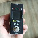 Černý kytarový ladič v kompaktním kovovém provedení. Na přední straně je displej, tři kontrolky a nápisy MiniTune a Vivlex. V horní části je označení…