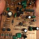Fotografie zachycuje hnědou tiskovanou plošnou desku s osazenými elektronickými součástkami, jako jsou rezistory, kondenzátory a tranzistory. Na desc…