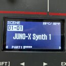 Detailní záběr na modrý displej elektronického nástroje. Na obrazovce je text SCENE 01-01, JUNO-X Synth 1 a v dolní části PART1. V pravém horním rohu…