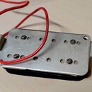Fotografie zachycuje spodní stranu elektrického snímače s kovovým krytem stříbrné barvy. K snímači vede červený elektrický kabel. Povrch kovového kry…