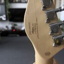 Zadní strana hlavy kytary z přírodního světlého dřeva s chromovanými ladičkami. Na dřevě jsou nápisy „Vintage a John Hornby Skewes Product®“, „Coaste…