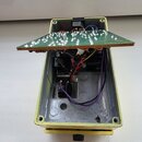 Fotografie zachycuje otevřený efekt pedál v žlutém kovovém šasi. Uvnitř je vidět elektronický plošný spoj s připájenými součástkami, který je mírně n…