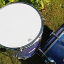 Fotografie zachycuje dva modré bubny s třpytivým povrchem umístěné na trávě. Na bílém koženu menšího bubnu je černý nápis „EVANS EC2 CLEAR DRUMHEAD“.…