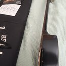 Fotografie zachycuje část akustické kytary v tmavě hnědé barvě, černý obal a doprovodné dokumenty. Na manuálu je viditelné logo Gibson a nápis OWNER'…