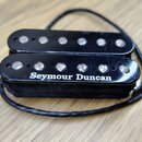 Černý humbucker s dvěma řadami magnetických pólů. Na spodním snímači je bílý nápis Seymour Duncan. Povrch plastového krytu vykazuje drobné škrábance…