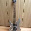 Stříbrná elektrická kytara s tmavým hnedým hmatníkem. Na hlavě je bílý nápis YAMAHA. Kytara má dva černé humbuckery, tremolo mechanismus a je umístěn…