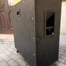 Černý kytarový reproduktor v texturovaném krytí s kovovými rohy. Na pravém boku je umístěna úchytka s nápisem Marshall a na levém boku je vidět připo…