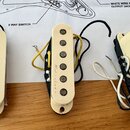 Tři kytarové snímače s krémovými plastovými kryty a viditelnými magnetickými póly. Na boku každého krytu je kurzivním písmem nápis „Novartone“. Sníma…