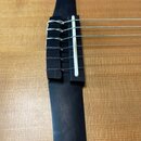 Detailní záběr na kobylku akustické kytary z tmavého dřeva s bílou kostěnou nebo plastovou vložkou. Na kobylku jsou upevněny šest kytarových strun po…