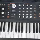 Černý synthesizér s klaviatura. Na levé straně je nápis HYDRASYNTH a logo ASM ASHUN SOUND MACHINES. Panel obsahuje množství ovládacích knoflíků, tlač…