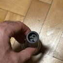 Detailní pohled na spodní část mikrofonu s konektorem XLR. Jsou vidět tři kovové piny v kulatém hrdle šedé barvy. Na fotce nejsou žádné viditelné zna…