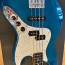 Modrá elektrická basová kytara s výraznou strukturou dřeva a bílo-perleťovým pickguardem. Na těle jsou dva snímače, jeden jednoduchý u kobylky a jede…