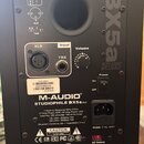 Zadní strana černého studiového monitoru. Je na něm vidět logo M-AUDIO a název modelu STUDIOPHILE BX5a DELUXE, v horní části je velký nápis BX5a DELU…