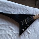 Černá elektrická kytara s ostrým, špičatým tvaru těla. Nástroj má dva snímače typu humbucker, stříbrný most a tři ovládací knoflíky. Hmatník je vyrob…
