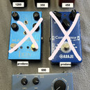 Fotografie zobrazuje pět kytarových efektů. V horní řadě jsou tři pedály: černý s nápisy „EHX-2020“ a „electro-harmonix“, černý s nápisy „ECHO RAIN“…