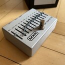 Stříbrný kytarový pedál s kovovým povrchem a stoupací spínačem. Na horním panelu je nápis MXR® a text "en band eq". Zařízení obsahuje řadu posuvníků…