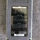 Zadní strana efektového pedálu s šedým kovovým šasi. Na zadní straně je černá náleplka s tabulkou BOSS AC ADAPTOR, varovnými texty v japonštině a ang…