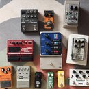 Fotografie zobrazuje skupinu jedenácti efektových pedálů pro kytaru a basu. Mezi nimi jsou značky Boss (modely RV-200, DS-1), Ibanez (model PD7 PHAT-…