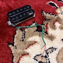 Černý humbucker s dvěma řadami magnetických pólů v kovovém rámečku. Na povrchu je bílý nápis XH 2. Z nástroje vede zelený kabel s odkrytými červeným…