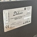 Detail stříbrného typového štítku na černém texturovaném povrchu kytarového komba. Na štítku je uveden model Hot Rod Deluxe a výrobce FENDER MUSICAL…