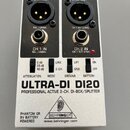 Stříbrná DI-box s černým horním panelem. Na zařízení jsou nápisy ULTRA-DI DI20, PROFESSIONAL ACTIVE 2-CH. DI-BOX/SPLITTER a logo BEHRINGER s webovou…
