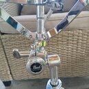 Detail chromovaného stojanu na bicí. Na kulatém prvku je viditelné logo Pearl a nápis HYRO-LOCK SYSTEM. Povrch je lesklý, s viditelnými odlesky a mír…