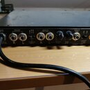 Zadní strana černého elektronického zařízení s několika konektory a přepínači. Jsou zde nápisy MAINS INPUT, MASTER OUTPUT s označením R a L, NOMINAL…