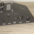 Černý elektronický přístroj s nápisem OPUS na horní straně. Zadní panel obsahuje konektory s popisky MIDI IN, AUX IN, DI OUT a LINE OUT, dále přepína…