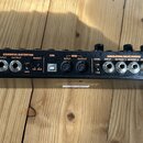 Zadávací panel černého elektronického zařízení s oranžovými nápisy. Jsou zde viditelné vstupy a výstupy s popisky EXP.PEDAL, OVERDRIVE/DISTORTION (IN…