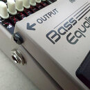 Detailní pohled na šedý efekt pedál s nápisy Bass Equalizer a GEB-7. Na horní části je vidět bílý knoflík a nápis OUTPUT se šipkou směřující doleva.…