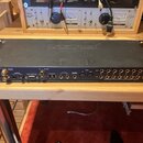 Černý rackový audio rozhraní s kovovým šasi. Na zadní straně jsou různé konektory a nápisy, včetně "WORD CLOCK", "S/PDIF", "ADAT SYNC IN", "FIREWIRE"…