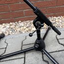Černý kovový stativ s rozkládacími nohami. Na spodním utahovacím knoflíku je vidět bílý nápis K&M. Povrch laku vykazuje drobné oděrky a známky použív…