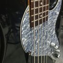 Černá elektrická basová kytara s hnedým hmatníkem. Nástroj má světle modrý vlnitý pickguard a chromované potenciometry. Na fotce nejsou žádné viditel…