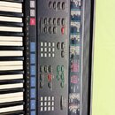 Černý digitální klavír s ovládacím panelem a bílo-černými klávesami. Na panelu jsou viditelné nápisy DIGITAL REVERB, AUTO BASS CHORD, CUSTOM ACCOMPAN…