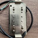 Elektrický snímač s kovovým krytem stříbrné barvy a černým tělem. Na krytu je vyryt nápis „Bare Knuckle Pickups“ a „Handwound in the UK“. Snímač má d…