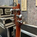 Zadní strana hlavy hnědé kytary s kovovými ladičkami. Na zadní straně hlavy je nápis: "Built by Cort Guitars Indonesia / Manufactured for Ibanez Co.,…