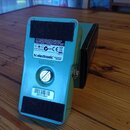 Zadní strana modrého efektového pedálu. Na štítku jsou nápisy MANUFACTURED IN FINLAND, tc electronic DESIGNED IN DENMARK a označení BATTERY. Dole je…