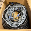 V kartonové krabici se nachází několik svázaných audio kabelů v černé a šedé barvě. Kabely mají kovové konektory s modrými plastovými krytkami. Na še…