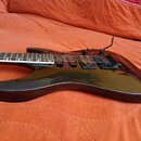 Černá elektrická kytara s lesklým povrchem a tmavou hmatníkem. Nástroj je vybaven dvěma humbuckery, Tremolo systémem a ovládacími knoflíky. Na těle n…