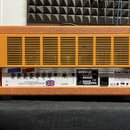 Zadní strana kytarového komba v oranžovém vinylu s černými hranami. Na bílém zadním panelu jsou nápisy ORANGE, ROCKERVERB 50 a AMPLIFIER HEAD. Jsou z…