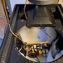 Černý reproduktorový box s otevřenou horní částí, v němž je vidět vnitřní zapojení s kondenzátory a cívkami na desce. Na horní straně boxu je umístěn…