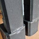 Dvě černé aktivní reproboxy umístěné na dvou černých subwooferech. Všechny čtyři komponenty mají kovové ochranné mřížky a v pravém dolním rohu nápis…