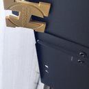 Detail černé kovové konstrukce s připevněným zlatým plastovým prvkem ve tvaru stylizedého písmene H. Na prvku je vyražen nápis HERCULES® STANDS. Povr…