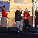 Fotografie zachycuje pět zpěváků na pódiu, z nichž čtyři drží v rukou mikrofony. V popředí jsou rozmístěny čtyři černé podiový monitorové reproduktor…