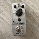 Stříbrný kytarový pedál s nápisem Groove Loop a značkou MOOER. Na horní straně se nachází černý ovládací knoflík s výběrem stylů (např. Rock, Fusion1…